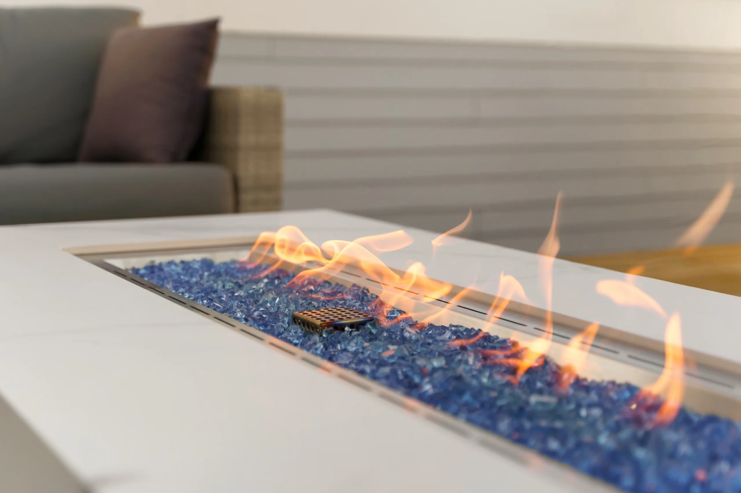 Fire table burning low over blue glass, the deck sofa soft behind the flames