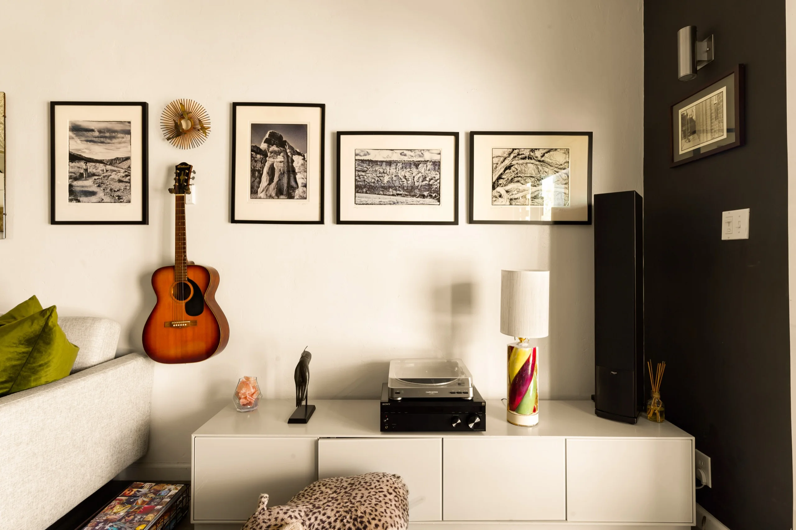 Row of framed black-and-white desert prints above a white console, an acoustic guitar and a record player below