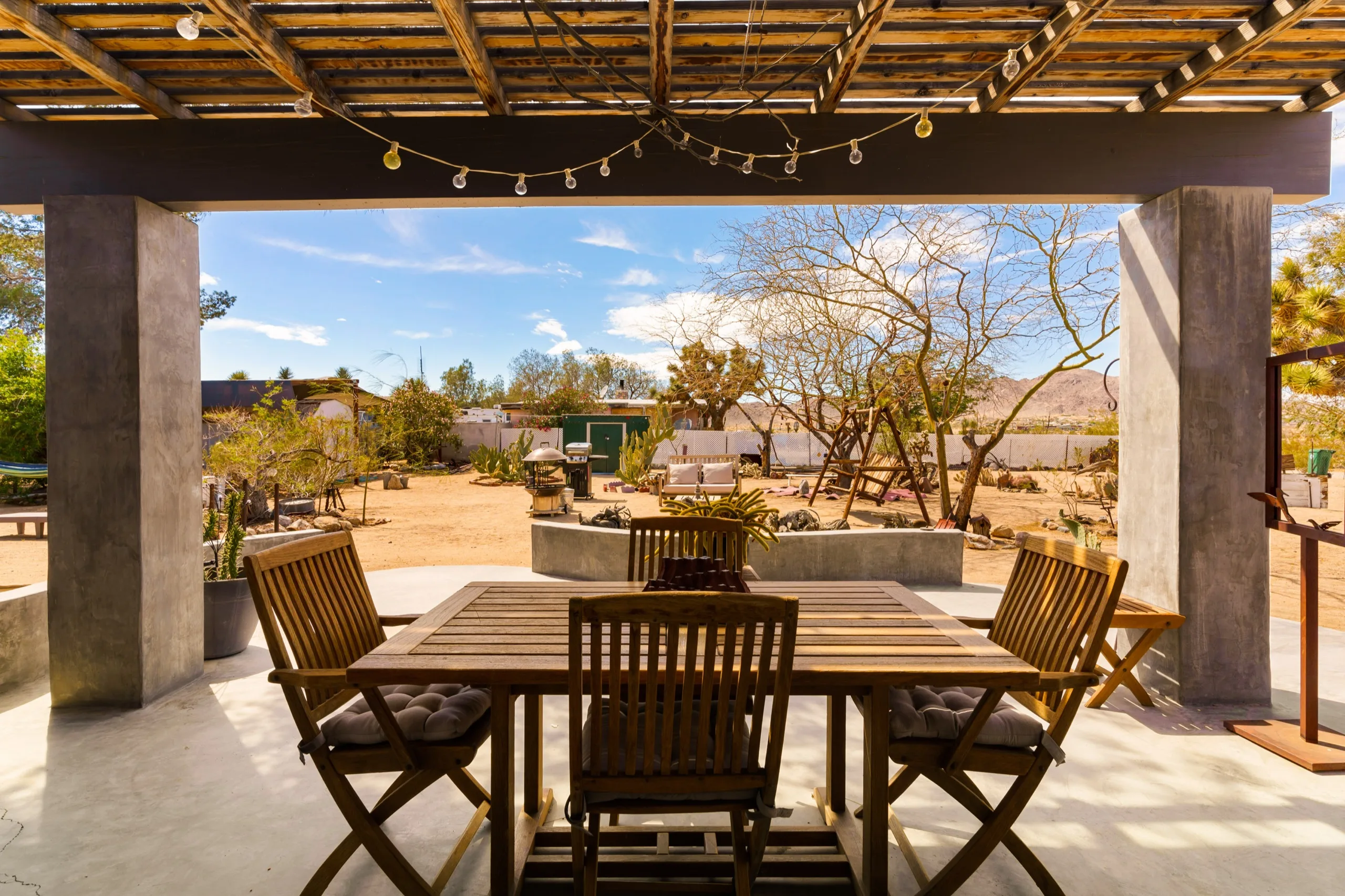 Timber pergola casting striped shadows over a dining table on a desert terrace