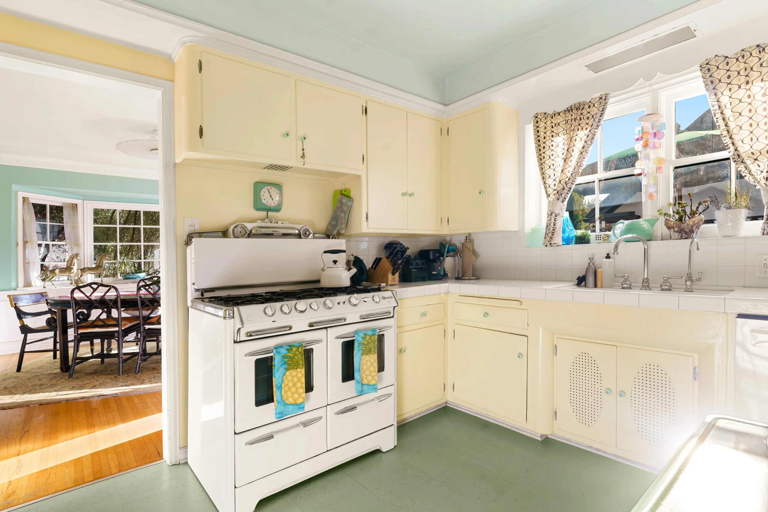 Period kitchen in butter yellow and mint, a vintage range beside a tiled counter and a window over the sink