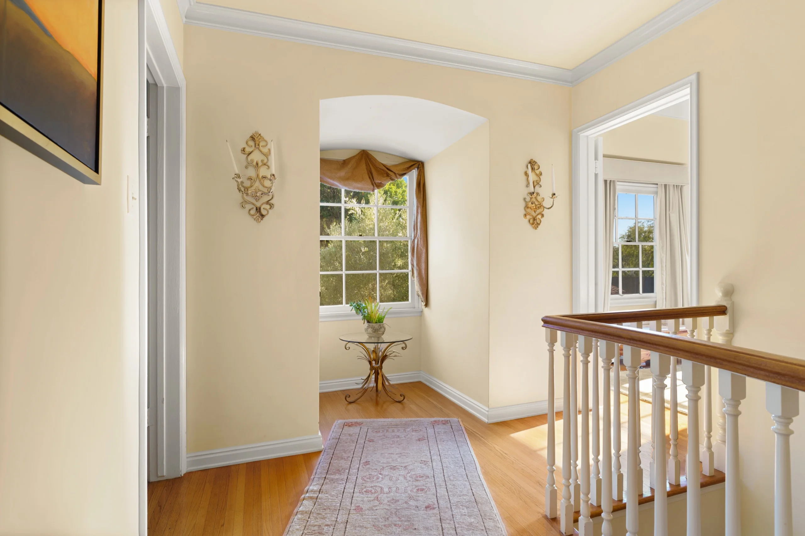 Upstairs landing with an arched alcove, brass sconces and a turned banister above the stair