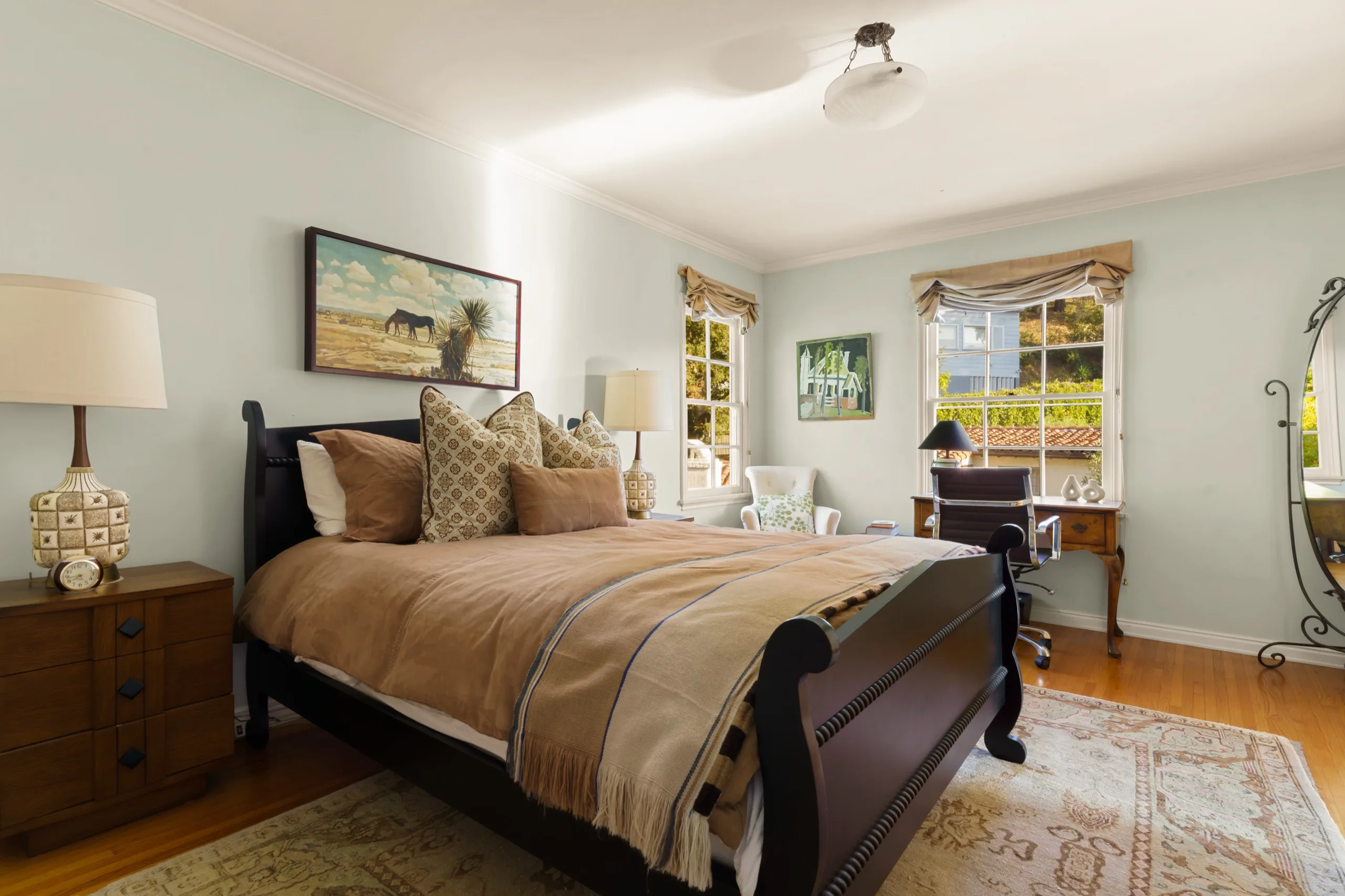 Bedroom in pale green with a dark sleigh bed, a writing desk set into the bay window