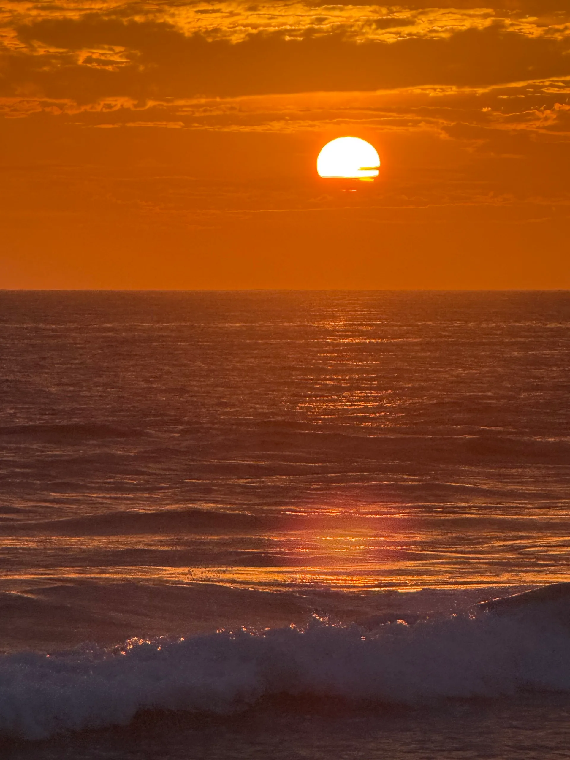 Large orange sun dropping to the horizon over breaking ocean swell