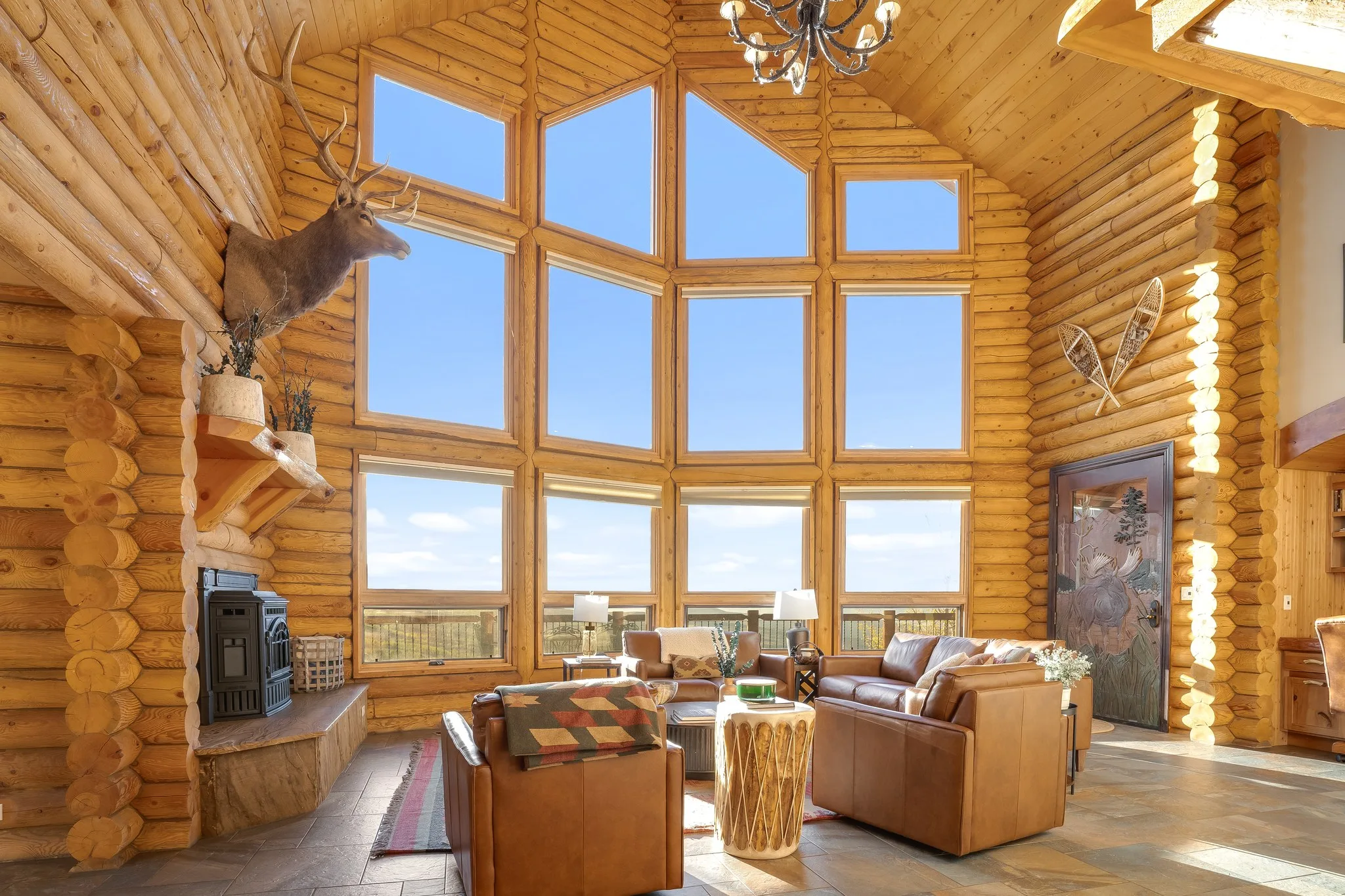 Great room seen from the entry, log walls rising to a vaulted ceiling and a wall of windows over the valley